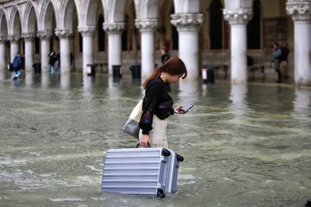 A tourist carries her luggage in a flooded St. Mark's Square, in Venice, Wednesday, November 13, 2019. The high-water mark hit 187 centimeters (74 inches) late Tuesday, Nov. 12, 2019, meaning more than 85% of the city was flooded. The highest level ever recorded was 194 centimeters (76 inches) during infamous flooding in 1966. (Photo by Luca Bruno/AP Photo)