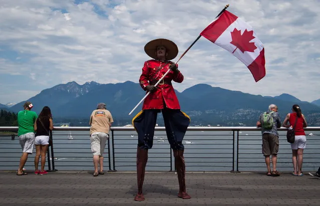 Dressed a Royal Canadian Mounted Police officer, Stephane Delage carries a Canadian flag while on stilts as he entertains the crowd during Canada Day festivities in Vancouver, B.C., on Monday, July 1, 2013. (Photo by Darryl Dyck/The Canadian Press)