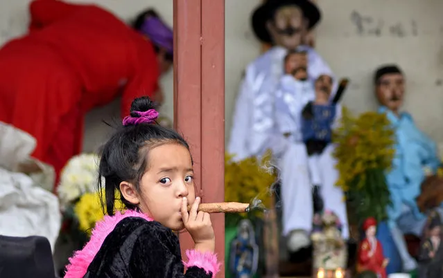A three-year-old girl smokes a cigar during the Saint Simon celebrations in San Andres Itzapa, Guatemala, on October 28, 2019. Thousands believe that the saint helps people find work, solves family problems and cures illnesses. (Photo by Orlando Estrada/AFP Photo)