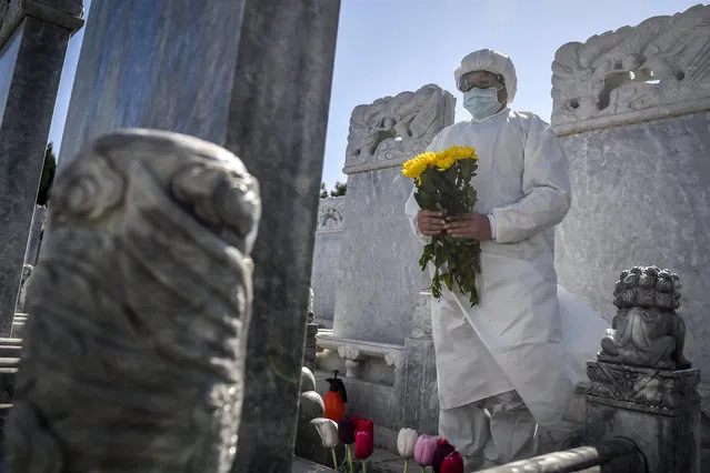 In this Saturday, March 28, 2020, photo released by Xinhua News Agency, a cemetery worker in a protective suit makes an offering of flowers at a grave site in the Babaoshan cemetery in Beijing. People can ask the cemetery to help clean up the tombs and place flowers and offerings to their deceased relatives during the Qingming Festival, which falls on April 4 this year, to prevent the normally large family gatherings following the new coronavirus outbreak. (Photo by Peng Ziyang/Xinhua via AP Photo)