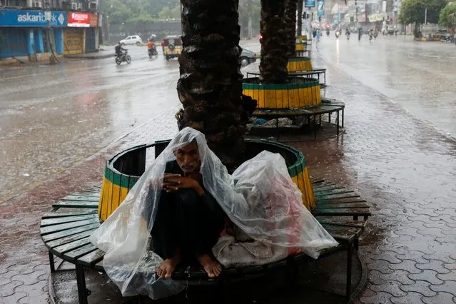 A man, covered with a plastic sheet to avoid rain, sits on a bench during the monsoon season, in Karachi, Pakistan on July 24, 2022. (Photo by Akhtar Soomro/Reuters)