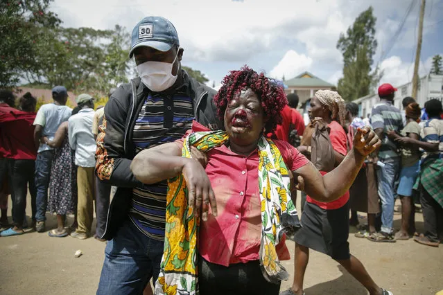 A woman who was injured after being trampled is helped away, after residents desperate for a planned distribution of food for those suffering under Kenya's coronavirus-related movement restrictions pushed through a gate and created a stampede, causing police to fire tear gas and leaving several injured, at a district office in the Kibera slum, or informal settlement, of Nairobi, Friday, April 10, 2020. (Photo by Brian Inganga/AP Photo)