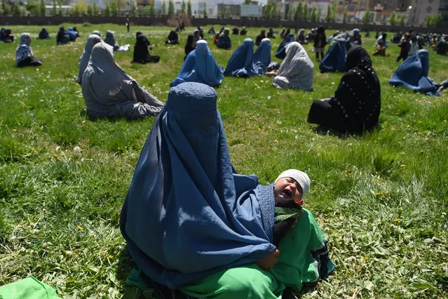 A woman wearing a burqa holds her child as she waits to receive free wheat from the government emergency committee during a government-imposed lockdown on the capital city as a preventive measure against the COVID-19 coronavirus, in Kabul on April 21, 2020. (Photo by Wakil Kohsar/AFP Photo)