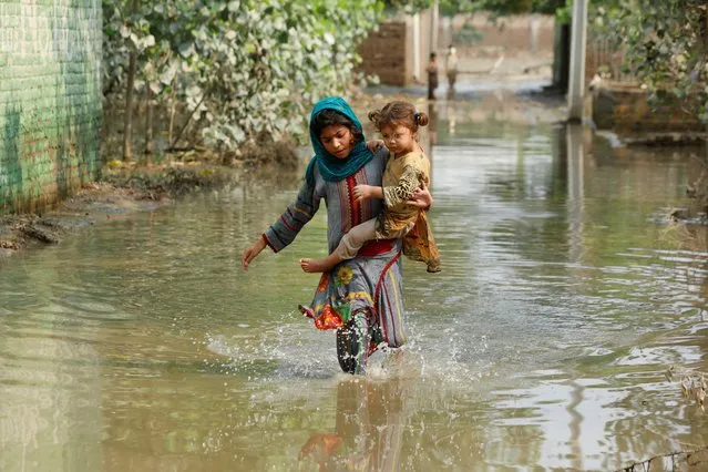A girl carries her sibling as she walks through stranded flood water, following rains and floods during the monsoon season in Nowshera, Pakistan on September 4, 2022. (Photo by Fayaz Aziz/Reuters)