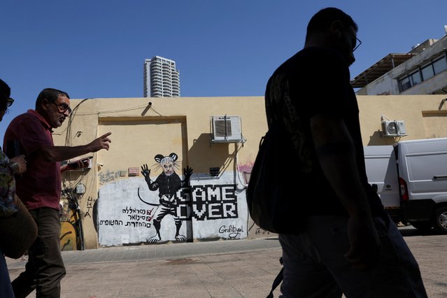 People walk past graffiti depicting the late Hamas leader Yahya Sinwar, in Tel Aviv, Israel, on October 20, 2024. The writing reads in Hebrew: “Nasrallah (check) Sinwar (check) Returning the hostages ( )” on October 20, 2024. (Photo by Violeta Santos Moura/Reuters)
