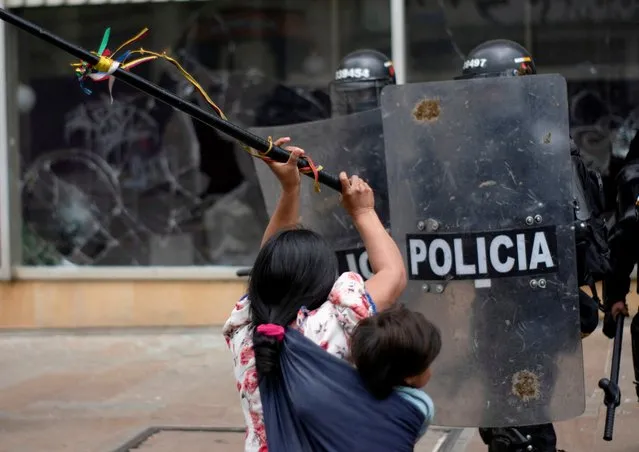 An Embera Indigenous woman carrying a child clashes with riot police while fighting for the right to land they say belongs to them, in Bogota, Colombia on October 19, 2022. (Photo by Harry Furia Grafica/Reuters)