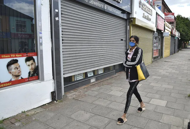 A woman wearing a mask to protect against coronavirus, walks in Melton Road also known as the Golden Mile in Leicester, England, Tuesday June 30, 2020. The British government has reimposed lockdown restrictions in the English city of Leicester after a spike in coronavirus infections, including the closure of shops that don't sell essential goods and schools. (Photo by Rui Vieira/AP Photo)