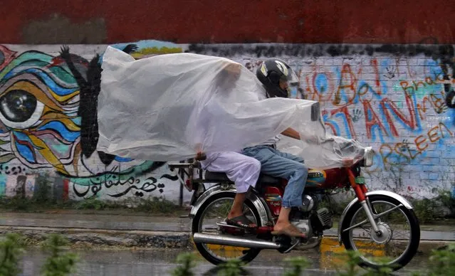 Pakistanis use a plastic sheet to protect themselves from rain in Rawalpindi, Pakistan, Wednesday, July 27, 2016. Monsoon season in Pakistan begins in July and ends in September. (Photo by Anjum Naveed/AP Photo)