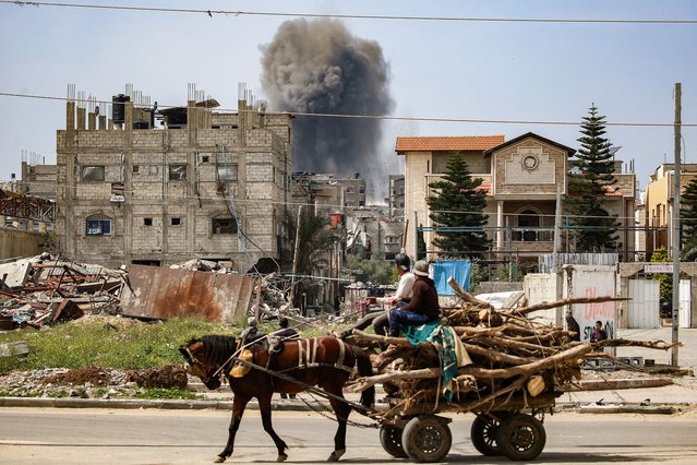 Men riding a horse-drawn cart carrying chopped tree branches for lumber watch as a smoke plume erupts from a building that was hit by Israeli bombardment after prior warning in the Nuseirat camp for Palestinian refugees in the central Gaza Strip on March 25, 2025. Israel, vowing to destroy Palestinian militant group Hamas, on March 18 resumed intense bombardment of Gaza and redeployed ground troops, shattering a truce that had largely held since January 19. (Photo by Eyad Baba/AFP Photo)
