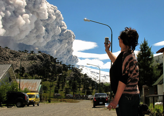 A woman takes a picture with her mobile phone from Caviahue, Neuquen province, Argentina, some 1500 km southwest of Buenos Aires, of the Copahue volcano spewing ashes on December 22, 2012. The authorities of Chile and Argentina issued yellow alerts due to the eruption of the Copahue volcano, placed in the border between both countries. (Photo by Antonio Huglich/AFP Photo)