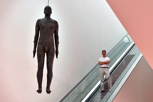 British artist Antony Gormley poses for a photograph next to his artwork entitled “Object, 1999”, a life-size cast-iron sculpture cast from the artist's body and hung from the ceiling of the National Portrait Gallery, during a press preview on September 7, 2016 in London, England. The work is accompanied on October 5 by “Fall, 1999”, a selection of drawings also by Mr Gormley. (Photo by Carl Court/Getty Images)