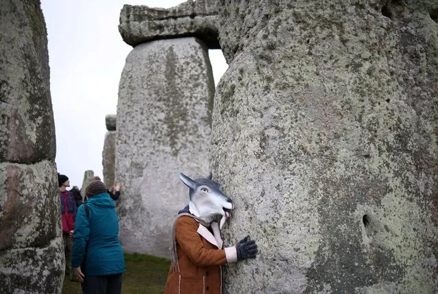 A person wearing an animal mask touches the stones during winter solstice celebrations at Stonehenge near Amesbury, Britain on, December 22, 2022. (Photo by Henry Nicholls/Reuters)