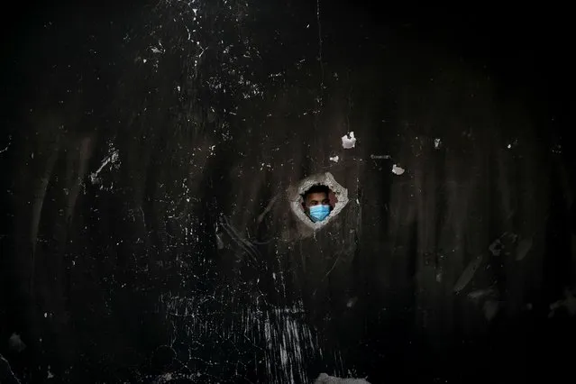 A Palestinian man wearing a protective face mask looks through a hole in a torched house where three children of Al-Hazeen family were killed in a fire ignited by a candle used to light up their room during a power cut in the central Gaza Strip on September 2, 2020. (Photo by Mohammed Salem/Reuters)