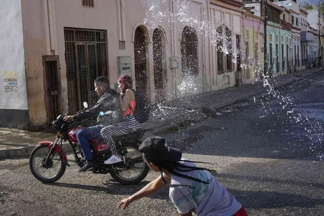 A couple on a motorcycle are drenched with water during carnival celebrations in the San Agustin neighborhood of Caracas, Venezuela, Monday, February 20, 2023. (Photo by Matias Delacroix/AP Photo)