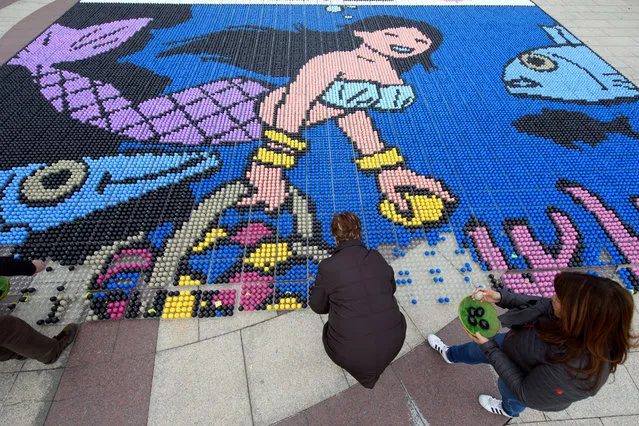 People disposes eggs of a easter mosaic of 39,780 dyed eggs, based on a drawing of the Swiss comics artist Cosey, during the 20th edition of the Easter Mosaic, in Lausanne Ouchy, Switzerland, 01 April 2018. 50,000 Swiss Francs were collected and will be given for the ARFEC association to help children with cancer and they family. (Photo by Laurent Gillieron/EPA/EFE)