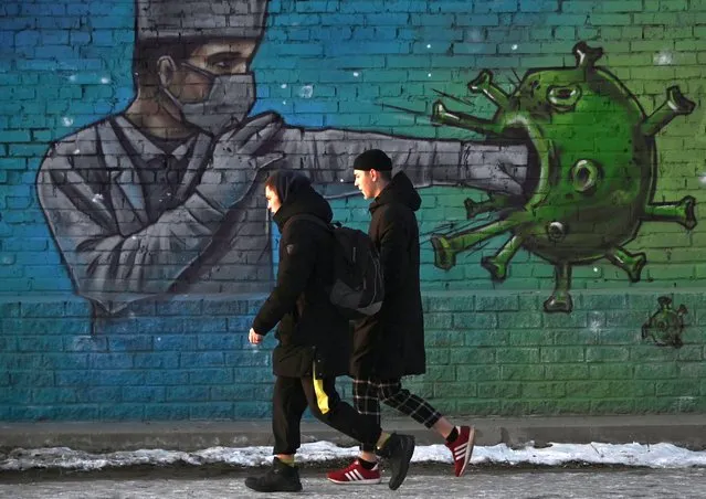 People walk past a graffiti depicting a healthcare worker fighting the virus, amid the outbreak of the coronavirus disease (COVID-19) in Omsk, Russia on November 23, 2020. (Photo by Alexey Malgavko/Reuters)