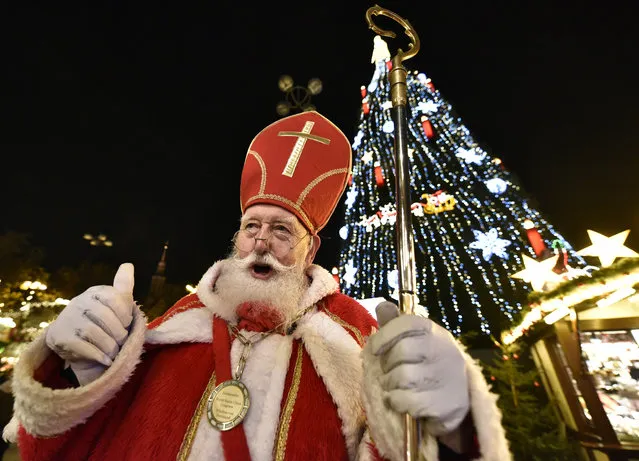 A man dressed as Santa Claus stands in front of Germany's biggest Christmas tree,  illuminated by 48,000 lights at the traditional Christmas market in Dortmund, Germany, Monday, November 23, 2015. The 45 meter high tree was built with 1,700 spruces and is a main attraction during advent season. (Photo by Martin Meissner/AP Photo)