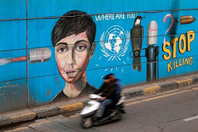 Men ride a scooter past a political graffiti mural criticising the United Nations along an underpass in Baghdad's Tahrir square on March 9, 2023. Twenty years after the US-led invasion of Iraq toppled Saddam Hussein, the oil-rich country remains deeply scarred by the conflict and, while closer to the United States, far from the liberal democracy Washington had envisioned. (Photo by Ahmad Al-Rubaye/AFP Photo)