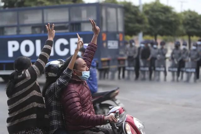 Protesters on a motorcycle flash the three-fingered salute as they drive past police in riot gear in Mandalay, Myanmar, on February 6, 2021. (Photo by AP Photo/Stringer)