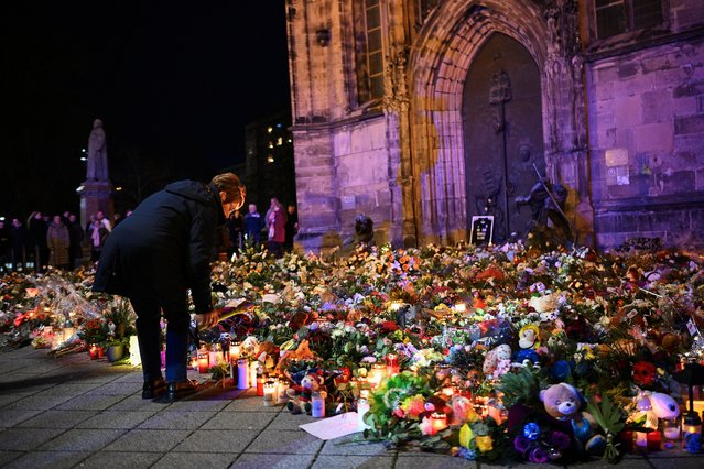 A woman bends to place a tribute with flowers and candles left near the 'Alter Markt' Christmas market, where a man drove a car into the crowd through an emergency exit route on Friday evening, in Magdeburg, Germany, on December 22, 2024. (Photo by Annegret Hilse/Reuters)