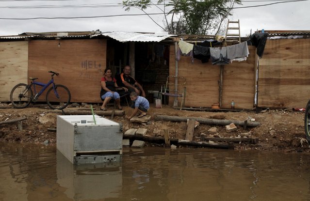 A family sits near flood waters in Asuncion, December 20, 2015. (Photo by Jorge Adorno/Reuters)
