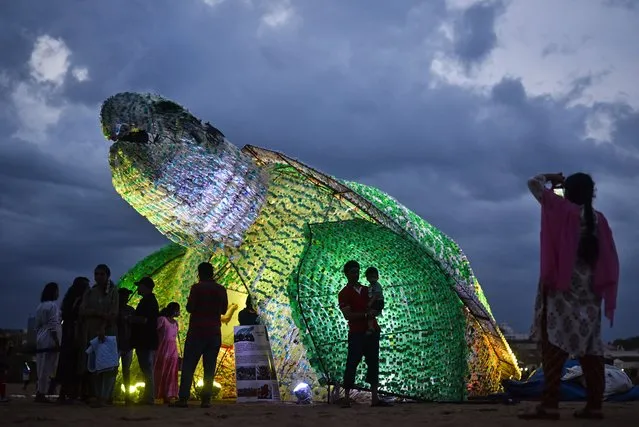 People stand near a huge replica of the green sea turtle made up of used plastic bottles to raise awareness among the public against the use of single-use plastic and its effect on marine life, at Edward Elliot's Beach in Chennai, India, 24 June 2023. The green sea turtle model made up of 600 kilograms of used plastic bottles was installed by Walk For Plastic (WFP), an environmental conservation organization, to create awareness among the public about plastic pollution's effect on marine life and to minimize the use of single-use plastic at Edward Elliot's Beach. (Photo by Idrees Mohammed/EPA)
