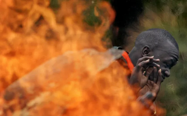 An opposition supporter shields his face from the flames of a burning makeshift roadblock in the village of Marura, near Eldoret, Kenya, Friday, January 18, 2008. (Photo by Ben Curtis/AP Photo)