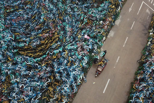 Urban management officers transport a bicycle next to piled-up bicycles of bike-sharing services in Hefei, Anhui province, China December 3, 2018. (Photo by Reuters/China Stringer Network)