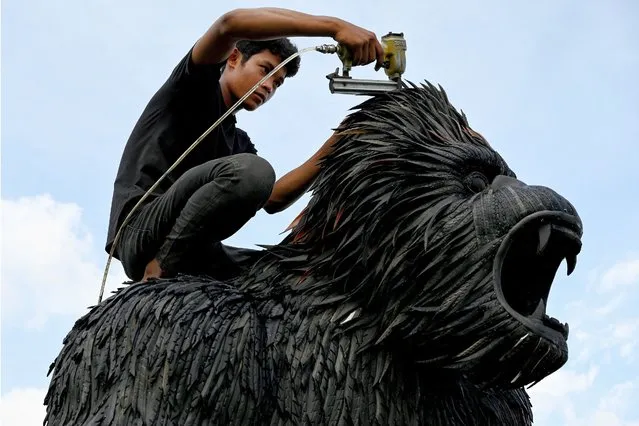 This photo taken on November 7, 2023 shows a worker fixing a King Kong statue made with old motorbike and bicycle tyres at artist Mean Tithpheap's house in Kandal province. Cambodian artist Mean Tithpheap has made some 40 statues for clients including King Kongs, elephants, lions, cobras, using bicycle and motorbike tyres with the hope of encouraging others to reuse materials in their work. (Photo by Tang Chhin Sothy/AFP Photo)
