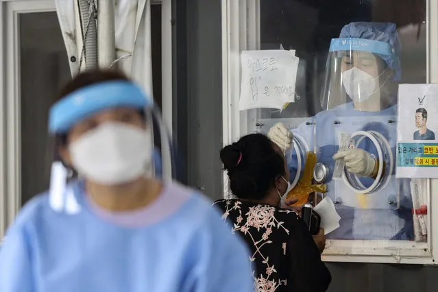 A medical worker wearing protective gear in a booth, takes sample from a visitor during a COVID-19 testing at a coronavirus testing site in Seoul, South Korea, Wednesday, August 11, 2021. (Photo by Im Hwa-young/Yonhap via AP Photo)
