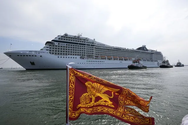 The the 92,409-ton, 16-deck MSC Orchestra cruise ship exits the lagoon as a flag of the Lion of St. Mark, the symbol of Venice, is being waved, in Venice, Italy, Saturday, June 5, 2021. The first cruise ship leaving Venice since the pandemic is set to depart Saturday amid protests by activists demanding that the enormous ships be permanently rerouted out the fragile lagoon, especially Giudecca Canal through the city's historic center, due to environmental and safety risks. (Photo by Antonio Calanni/AP Photo)