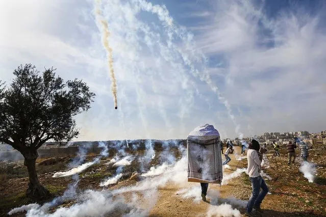 A man wearing a large puppet head and Palestinian stone-throwing protesters run as tear gas is fired by Israeli soldiers during clashes at a weekly demonstration against Jewish settlements in the West Bank village of Bilin, near Ramallah, on January 3, 2013. (Photo by Mohamad Torokman/Reuters)