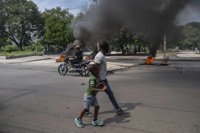 A man and a child walk by burning tires on a street in Port-au-Prince, Haiti, Sunday, October 17, 2021. (Photo by Joseph Odelyn/AP Photo)