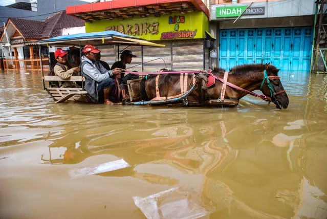 This picture taken on March 7, 2019 shows residents commuting along a flooded road in Dayeuhkolot village in Bandung, West Java province. Some 6,000 houses have been flooded from the overflowing Citarum river due to heavy rain in the area. (Photo by Timur Matahari/AFP Photo)