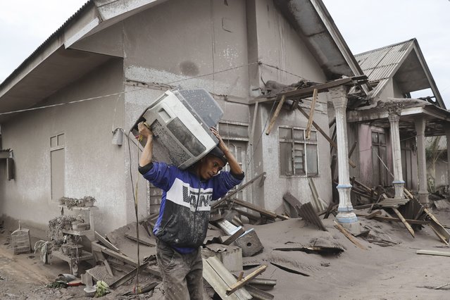 A man carries a television as he evacuates to a safer place following the eruption of Mount Semeru in Lumajang district, East Java province, Indonesia, Monday, December 6, 2021. The highest volcano on Java island spewed thick columns of ash into the sky in a sudden eruption Saturday triggered by heavy rains. Villages and nearby towns were blanketed and several hamlets buried under tons of mud from volcanic debris. (Photo by Trisnadi/AP Photo)