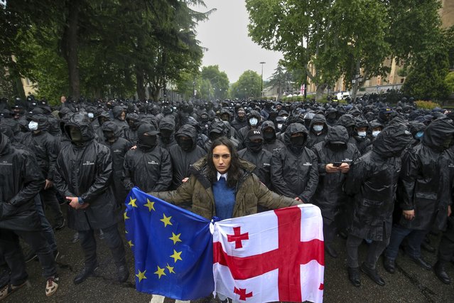 A woman holds a Georgian national and an EU flags in front of riot police blocking a street to prevent demonstrators during an opposition protest against “the Russian law” near the Parliament building in the center of Tbilisi, Georgia, Tuesday, May 14, 2024. The Georgian parliament on Tuesday approved in the third and final reading a divisive bill that sparked weeks of mass protests, with critics seeing it as a threat to democratic freedoms and the country's aspirations to join the European Union. (Photo by Zurab Tsertsvadze/AP Photo)