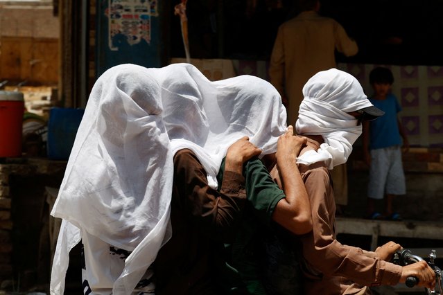 Men ride on a motorbike as they cover their heads with a wet cloth to cool off and to avoid sunlight, during a hot summer day, as the heatwave continues in Jacobabad, Pakistan on May 26, 2024. (Photo by Akhtar Soomro/Reuters)