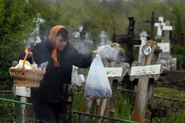 A woman burns incense in front of the graves of her relatives at a cemetery in the village of Copaciu, southwest of Bucharest, early morning April 17, 2014. Orthodox women went to church and cemeteries in the early morning on Maundy Thursday to light candles, burn incense and mourn their dead relatives as part of a southern Romanian tradition. Maundy Thursday, or Holy Thursday, is the day Christians commemorate the Last Supper of Jesus Christ. (Photo by Bogdan Cristel/Reuters)