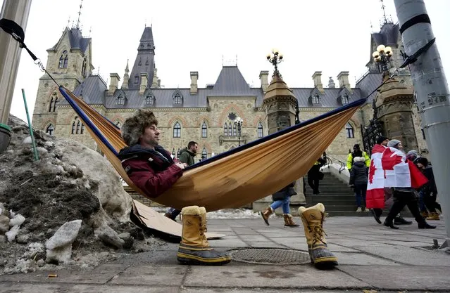 A man sits in a hammock outside West Block on Parliament Hill during a protest against COVID-19 restrictions in Ottawa, on Friday, February 11, 2022.  Ontario’s premier declared a state of emergency Friday in reaction to the truck blockades in Ottawa and at the U.S. border and threatened heavy penalties against those who interfere with the free flow of goods and people. (Photo by Justin Tang /The Canadian Press via AP Photo)