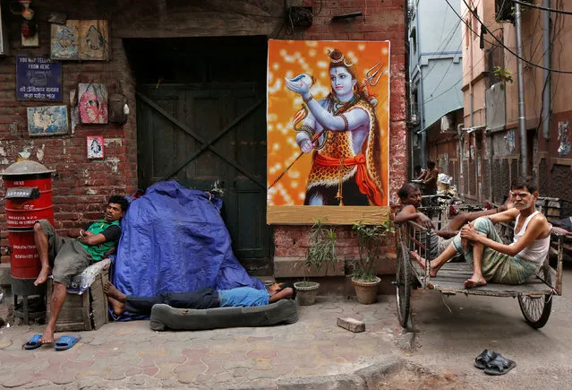 People rest beside a poster of Hindu Lord Shiva on a roadside in Kolkata, March 28, 2017. (Photo by Rupak De Chowdhuri/Reuters)