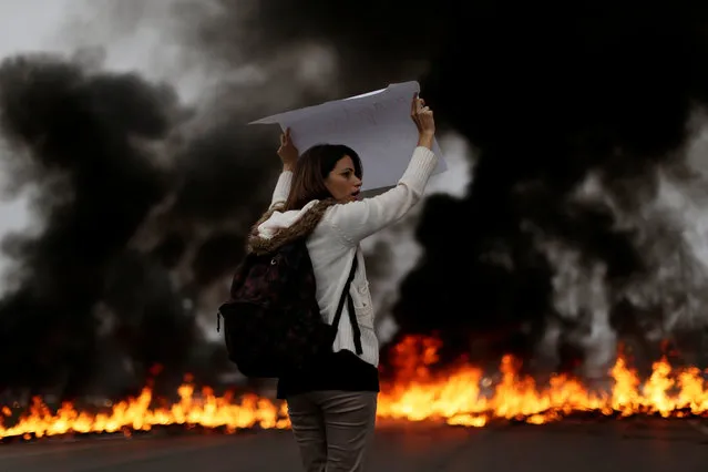 A demonstrators holds a placard in front of a burning barricade during a protest against President Michel Temer's proposal to reform Brazil's social security system in the early hours of general strike in Brasilia, Brazil, April 28, 2017. (Photo by Ueslei Marcelino/Reuters)