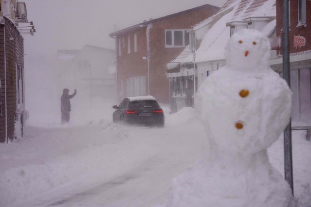 A car drives through a street where a huge snowman stands on the roadside during heavy snowfall in Hirtshals, northern Jutland, Denmark, on March 7, 2023. (Photo by Bo Amstrup/Ritzau Scanpix via AFP Photo)