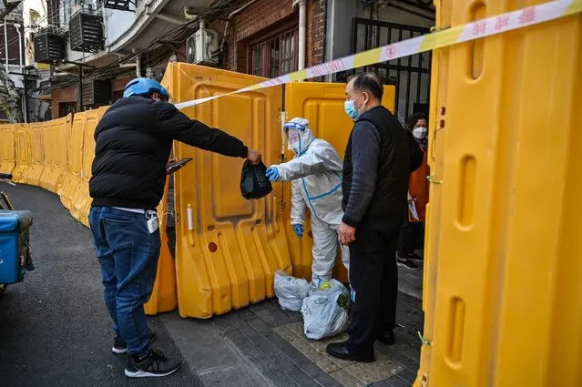 A worker, wearing a protective gear, guards the entrance to a neighborhood in lockdown as a measure against the Covid-19 coronavirus receive food from a delivery man, in Jing'an district, in Shanghai on March 29, 2022. (Photo by Hector Retamal/AFP Photo)