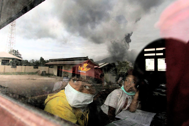 Primary school children wear masks while studying in the classroom in Karo district, North Sumatra province, on May 24, 2016, as Mount Sinabung is seen spewing out volcanic ash through the school window reflection. Indonesian rescuers searched for survivors in scorched villages and devastated farmlands after a volcano erupted in clouds of searing ash and gas, killing seven and leaving others fighting life-threatening burns. (Photo by Fatima Elkareem/AFP Photo)