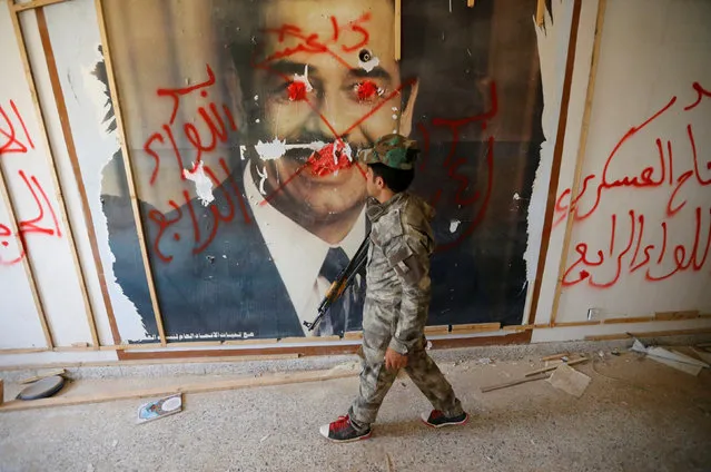 A fighters from the Iraqi Shi'ite Badr Organization looks at a poster depicting images of former Iraqi President Saddam Hussein on the outskirts of Falluja, Iraq, May 28, 2016. (Photo by Thaier Al-Sudani/Reuters)