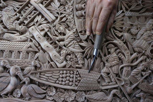 Ghulam Nabi Zargar, 70, a walnut wood carving artisan, points at detail showing a Kashmiri Shikara (boat) on a walnut wood piece that he prepares at his workshop in downtown Srinagar, the summer capital of Indian Kashmir, 31 July 2024. Zargar has been working as a walnut wood carving artisan for 53 years and is reviving the almost dying craft in Srinagar by inculcating creative and new designs including carvingsof the map of Srinagar City or route maps to the Hindu pilgrimage site Amarnath Cave. Only a handful of walnut wood carving artisans continue to keep the art in Kashmir alive. The craft has been passed down to them through generations, however, their next generations are not taking up the craft due to the financial constraints. The skill and mastery of the master wood carving craftsmen of Kashmir can be seen in four main types of carvings - raised, engraved, undercut, and plain. Kashmiri craftsmen rejoice in carving intricate and varied designs including those bearing recurrent motifs of the rose, lotus, iris, bunches of grapes, pears, Chinar leaves, and dragon motifs. (Photo by Farooq Khan/EPA)