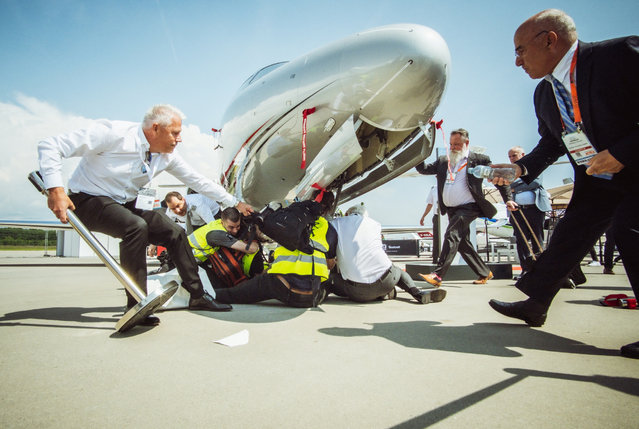 This handout picture taken and released on May 23, 2023 by Greenpeace shows unidentified people rushing to climate activists beneath a business jet during a protest at European business aviation show EBACE (European Business Aviation Convention & Exhibition) at Geneva Airport on May 23, 2023. Protesters on the tarmac at Geneva airport briefly disrupted air traffic before operations were gradually resumed, the airport said, as dozens of climate activists blocked a nearby business jet convention. (Photo by Thomas Wolf/GREENPEACEvia AFP Photo)