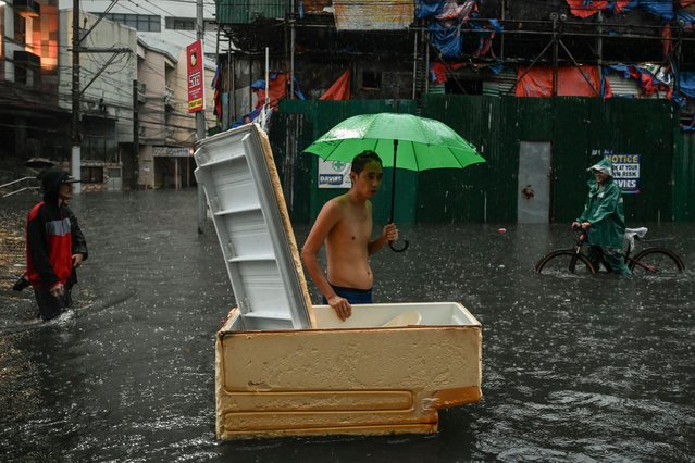 People walk along a flooded street in Manila on July 24, 2024 amid heavy rains brought by Typhoon Gaemi. Relentless rain drenched the northern Philippines on July 24, triggering flooding in Manila and landslides in mountainous regions as Typhoon Gaemi intensified the seasonal monsoon. (Photo by Jam Sta Rosa/AFP Photo)