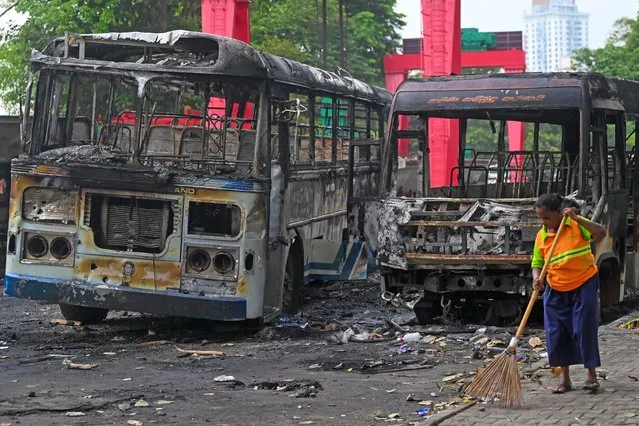 A worker sweeps the street alongside the burnt buses near Sri Lanka's former prime minister Mahinda Rajapaksa's official residence 'Temple Trees', a day after they were torched by protesters in Colombo on May 10, 2022. Five people were killed and more than 225 wounded in a wave of violence in Sri Lanka where the prime minister resigned after weeks of protests over the worsening economic crisis. (Photo by Ishara S. Kodikara/AFP Photo)
