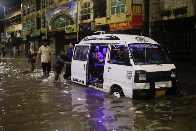 Men push a vehicle with their family on board on a flooded street, following heavy rains during the monsoon season in Karachi, Pakistan on July 24, 2022. (Photo by Akhtar Soomro/Reuters)